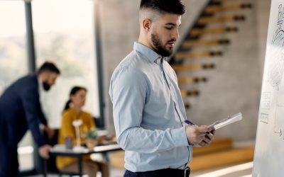 jeune-homme-affaires-lisant-notes-tout-dessinant-plan-tableau-blanc-au-bureau-edited-scaled